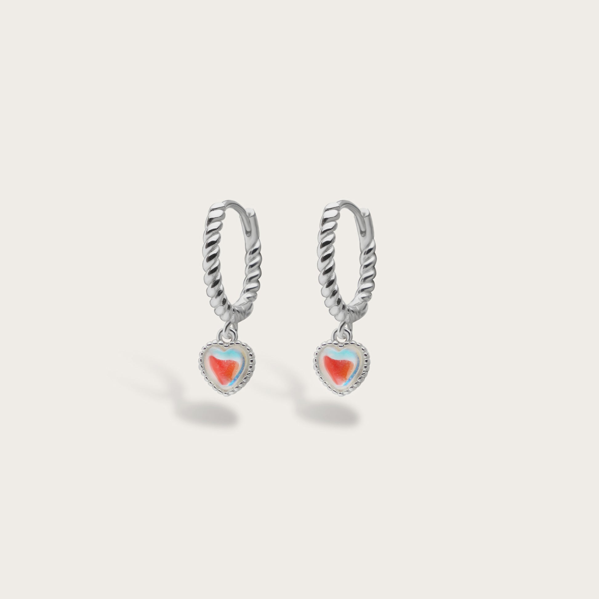 Silver hoop earrings with heart-shaped charms on a light gray background