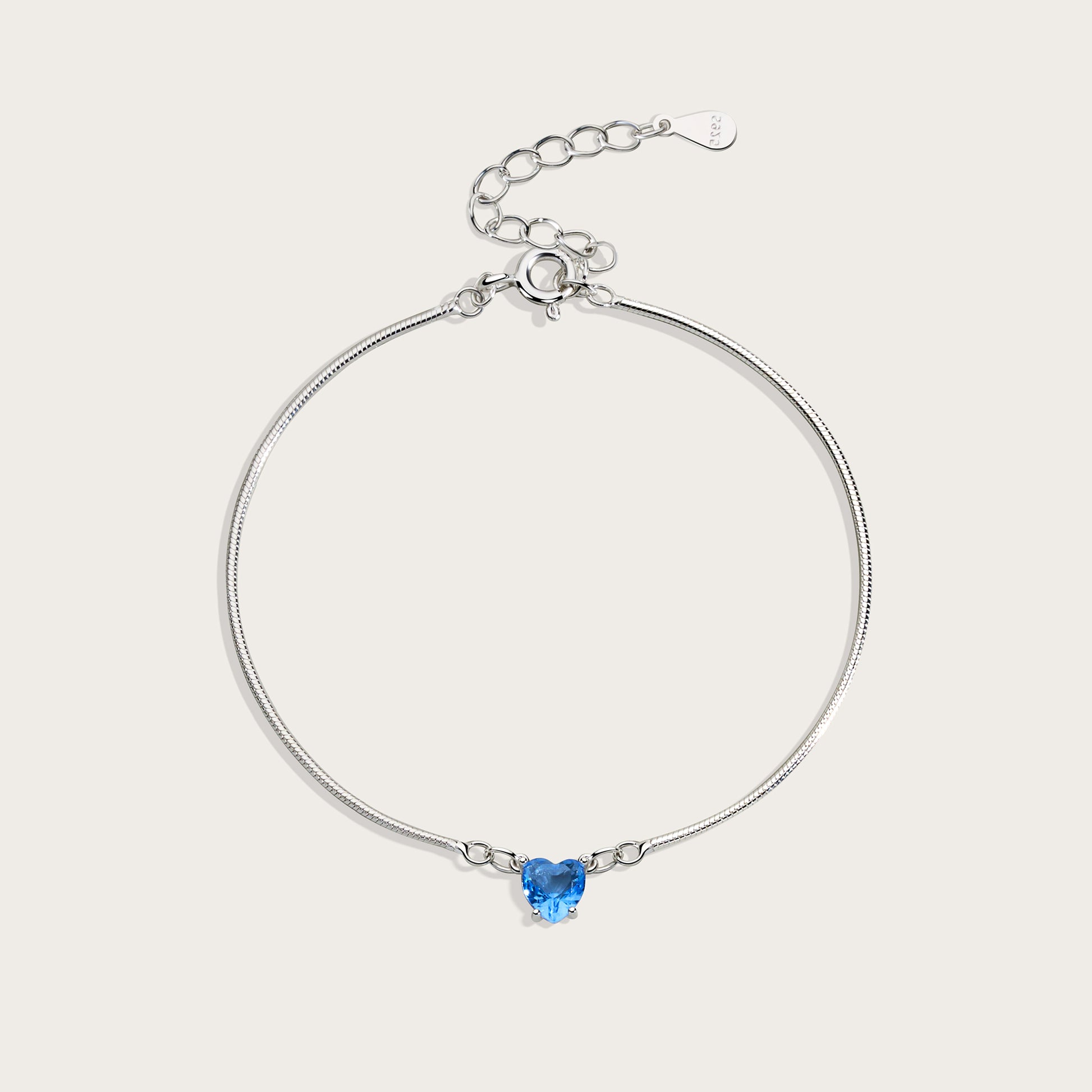 Silver bracelet with a heart-shaped blue gemstone on a light gray background