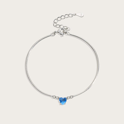 Silver bracelet with a heart-shaped blue gemstone on a light gray background