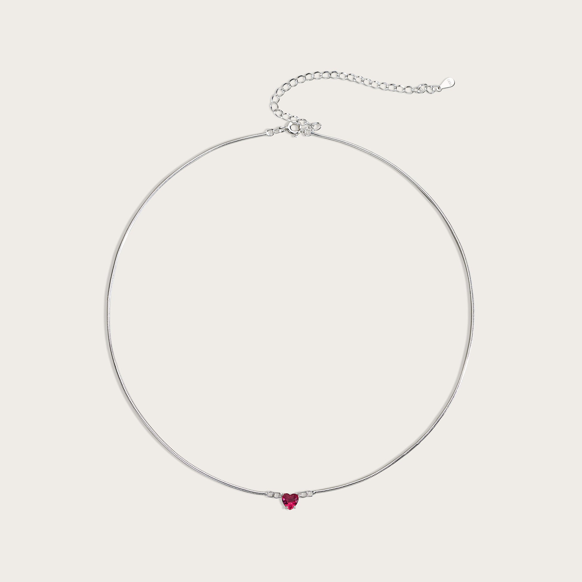 Silver necklace with a heart-shaped red gemstone on a light gray background